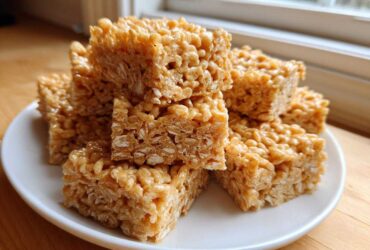 A stack of chewy No-Bake Peanut Butter Rice Cereal Bars piled high on a white plate.