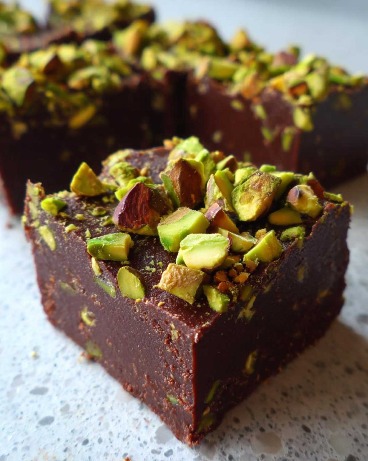 A close-up of a rich, dark chocolate No-Bake Pistachio Chocolate Fudge Squares topped with chopped green pistachios.