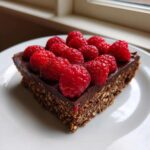 A single square serving of No-Bake Raspberry Chocolate Oat Slice topped with fresh raspberries.