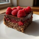 A single square serving of No-Bake Raspberry Chocolate Oat Slice topped with fresh raspberries.