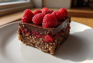 A single square serving of No-Bake Raspberry Chocolate Oat Slice topped with fresh raspberries.