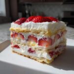 Close-up of a layered slice of No-Bake Strawberry Lemon Icebox Cake with whipped cream and fresh strawberries.