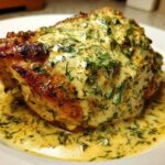 Close-up of a juicy chicken thigh covered in creamy lemon dill sauce and fresh dill.