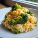 A close-up serving of One-Pot Creamy Broccoli Cheddar Rice topped with bright green broccoli florets and melted cheddar cheese.