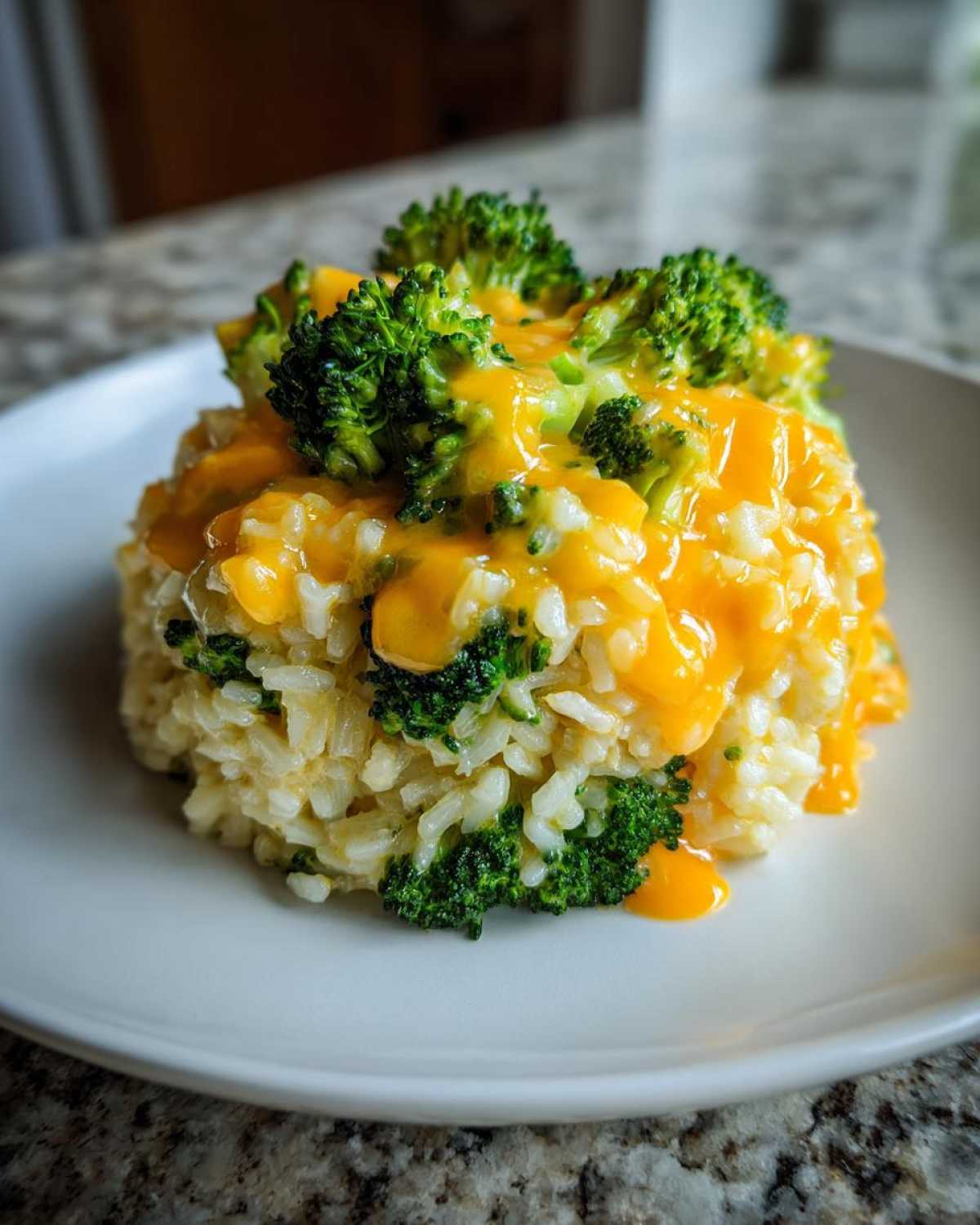 A molded serving of One-Pot Creamy Broccoli Cheddar Rice topped with melted cheddar cheese and fresh broccoli florets.