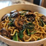 Close-up of One-Pot Creamy Mushroom Spinach Ramen noodles coated in sauce, topped with sliced mushrooms and sesame seeds.