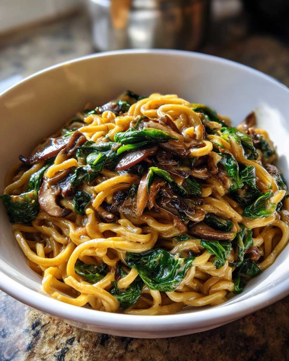 A close-up of One-Pot Creamy Mushroom Spinach Ramen served in a white bowl, featuring thick noodles, sautéed mushrooms, and wilted spinach.