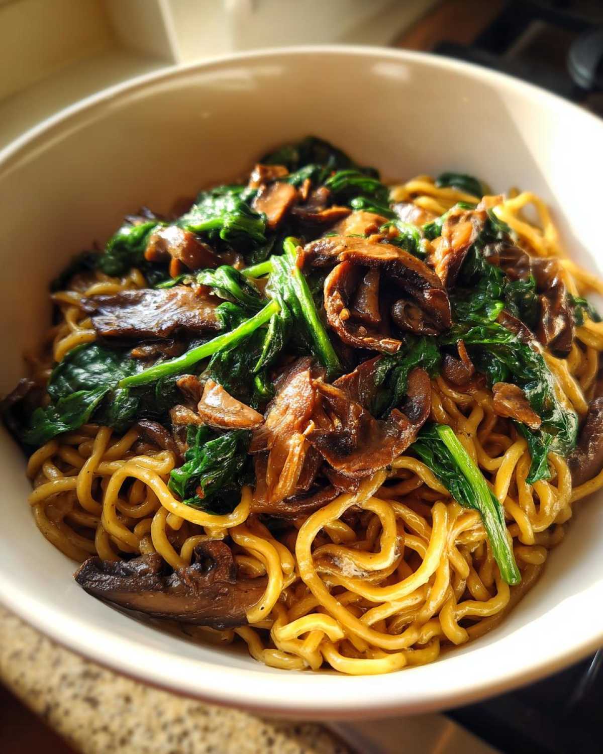 Close-up of a white bowl filled with One-Pot Creamy Mushroom Spinach Ramen, featuring golden noodles topped with sautéed mushrooms and wilted spinach.