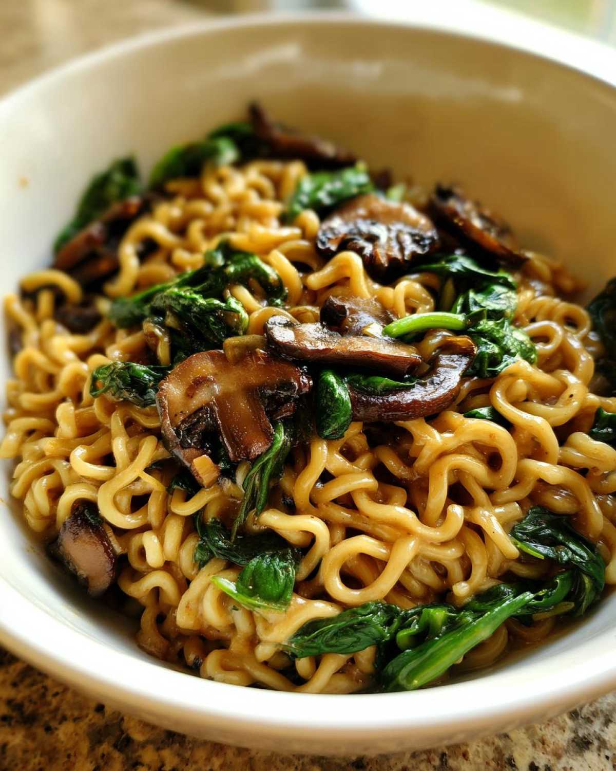 Close-up of One-Pot Creamy Mushroom Spinach Ramen noodles topped with sautéed mushrooms and wilted spinach.