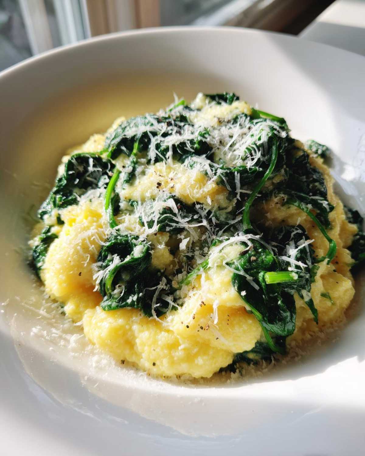 A close-up of One-Pot Creamy Spinach Parmesan Polenta topped with grated cheese and black pepper in a white bowl.