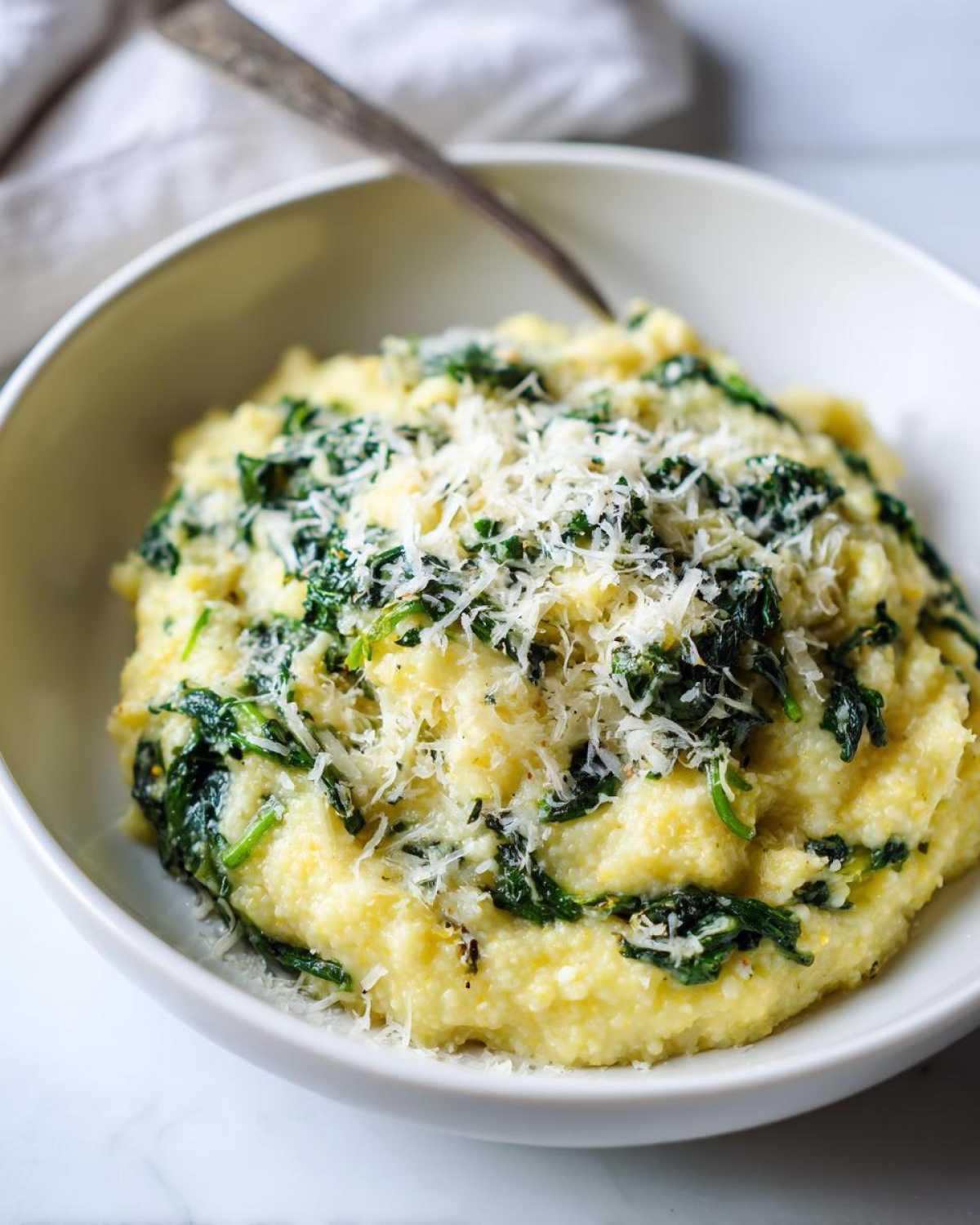 Close-up of One-Pot Creamy Spinach Parmesan Polenta topped with grated cheese in a white bowl.