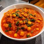 Close-up of a white bowl filled with rich, creamy One-Pot Creamy Tomato Basil Chickpea Stew, garnished with fresh basil.