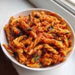 Close-up of a bowl filled with One-Pot Creamy Tomato Basil Tortilla Pasta, featuring fusilli pasta coated in a rich red sauce and fresh basil.