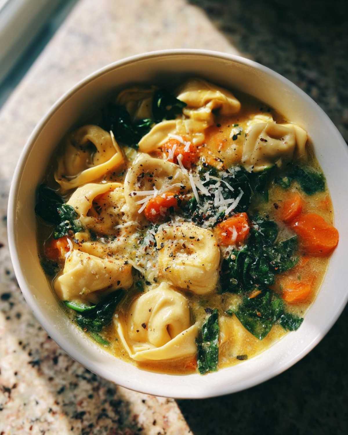 Overhead view of a white bowl filled with One-Pot Creamy Tortellini Minestrone soup, topped with Parmesan and pepper.