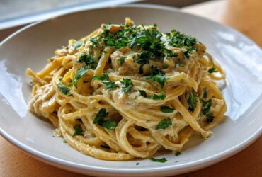 A close-up of One-Pot Creamy White Bean Lemon Pasta served in a white bowl, topped with fresh parsley.
