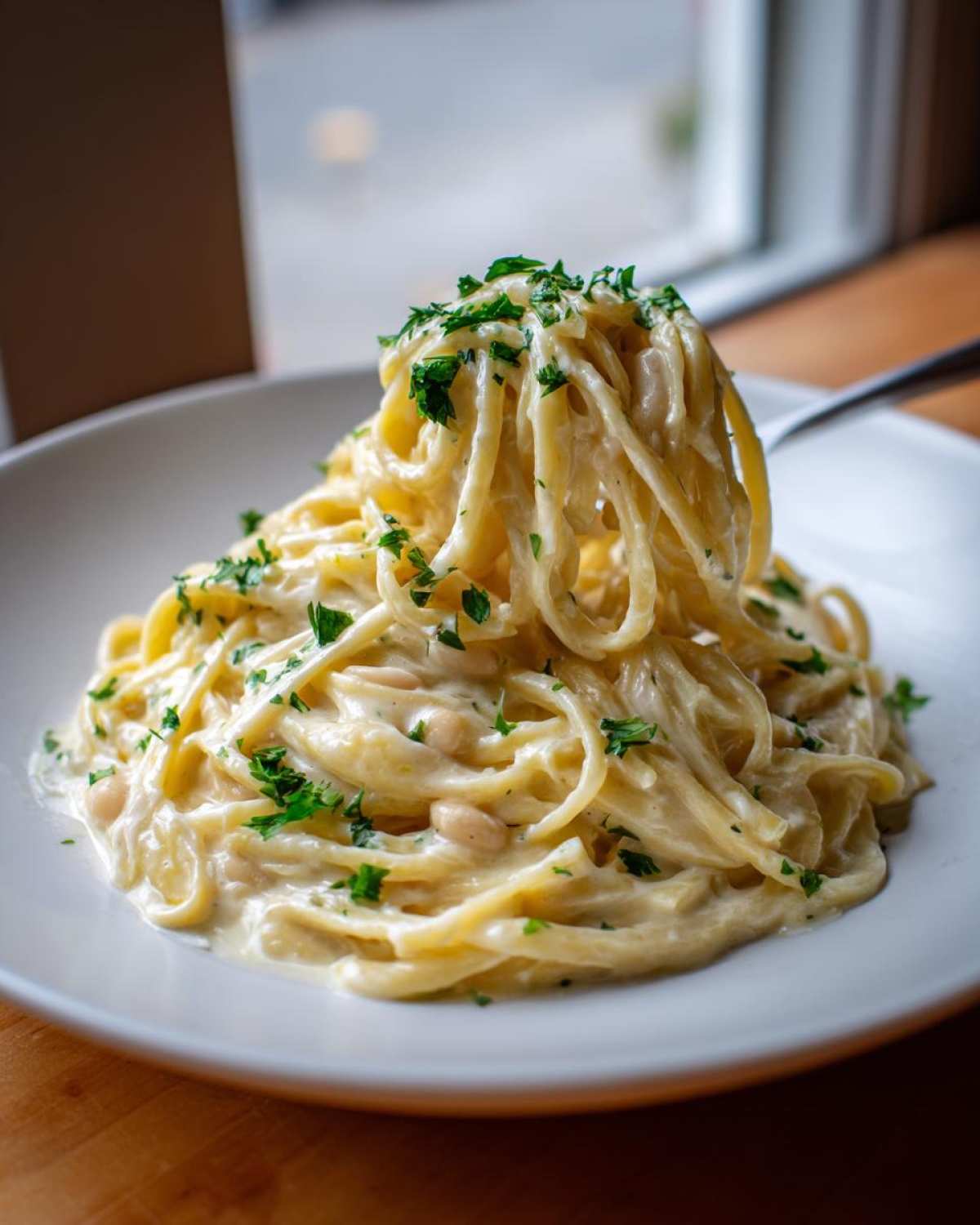 A fork twirls a large serving of One-Pot Creamy White Bean Lemon Pasta, topped with fresh parsley.