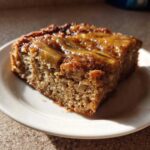 A square slice of Ooey Gooey Banana Bars with a shiny, caramelized banana topping on a small white plate.