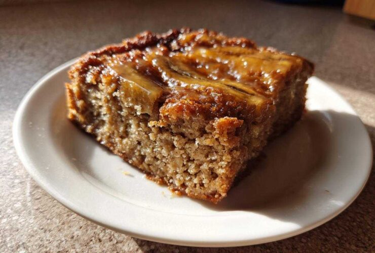 A square slice of Ooey Gooey Banana Bars with a shiny, caramelized banana topping on a small white plate.