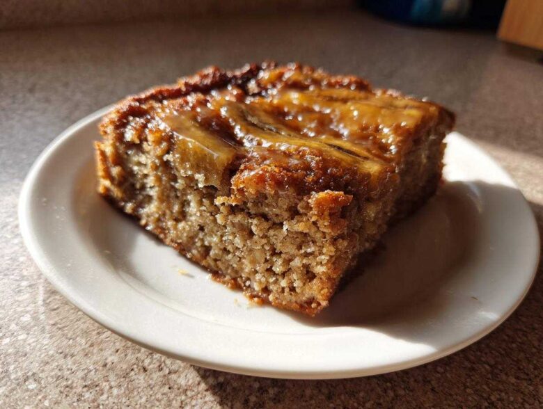A square slice of Ooey Gooey Banana Bars with a shiny, caramelized banana topping on a small white plate.