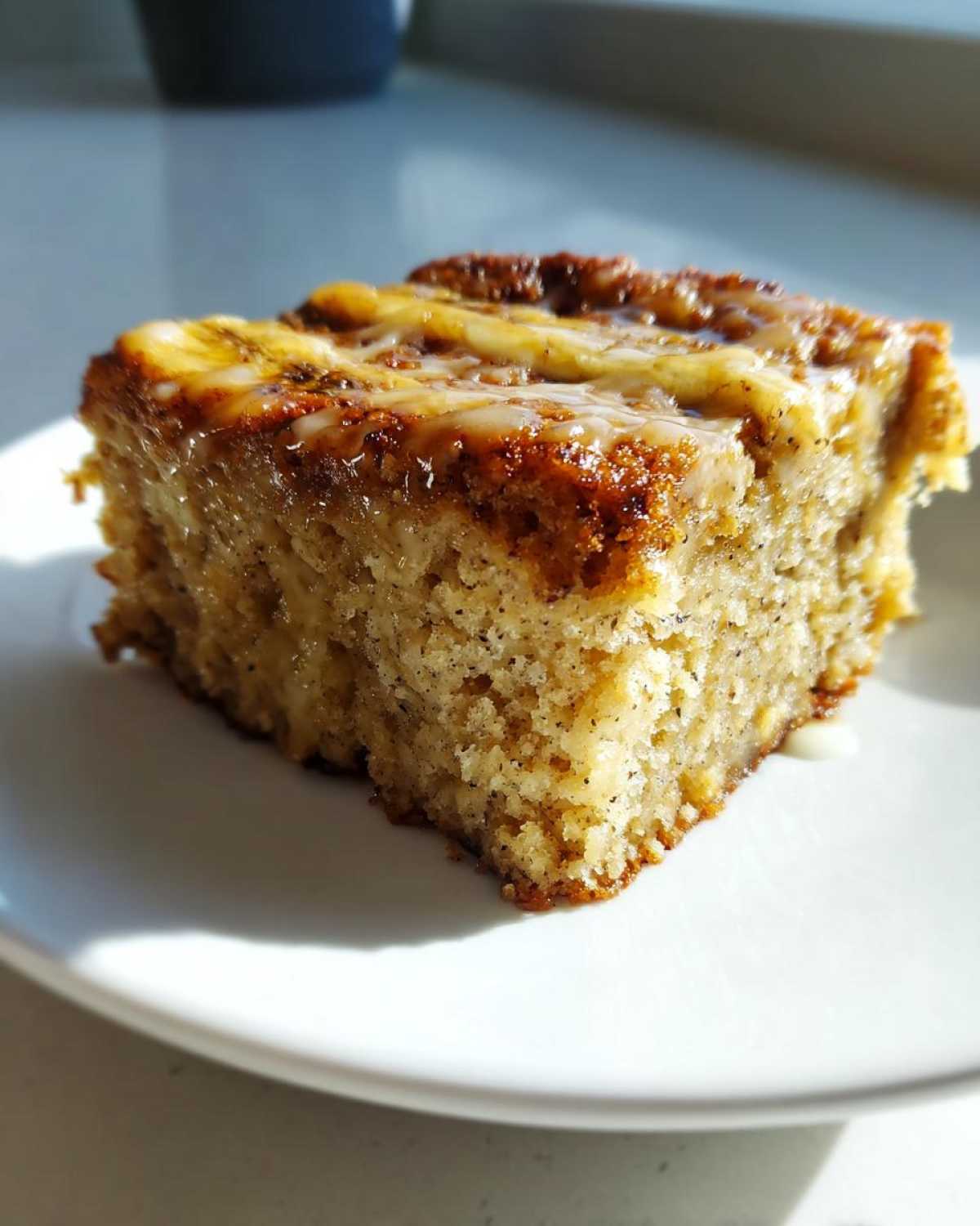 A moist square slice of Ooey Gooey Banana Bars topped with a sweet, dripping glaze, served on a white plate.