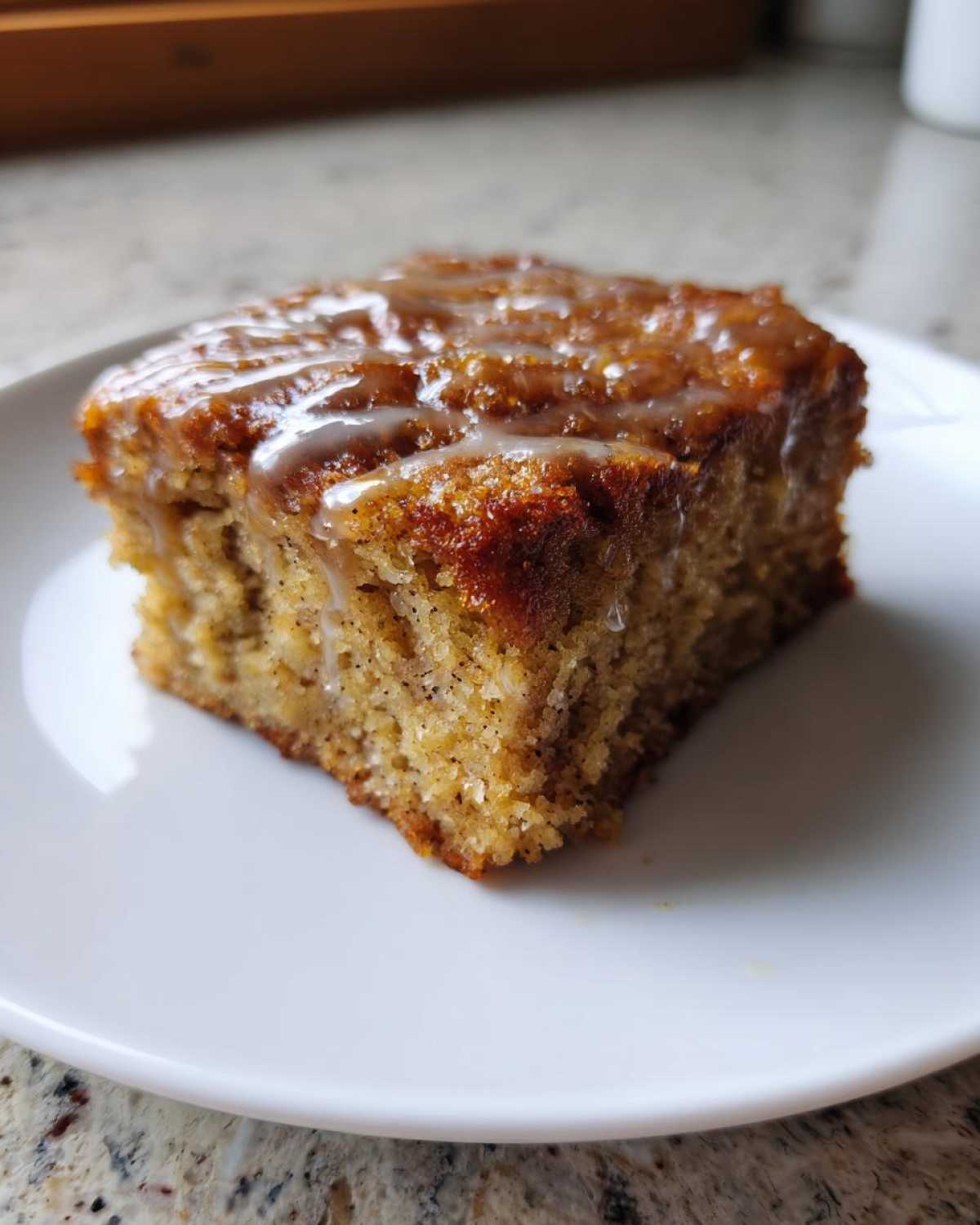 A single square of Ooey Gooey Banana Bars topped with a light, shiny glaze, served on a white plate.
