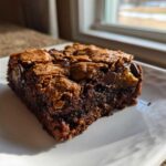 A single, rich, dark chocolate Ooey Gooey Bar with a crackly top and visible chocolate chips, resting on a white plate.