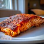 Close-up of a juicy Oven Baked Cajun Salmon fillet with a rich, dark red spice crust on a white plate.