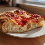 A thick slice of homemade pizza showing an airy, bubbly crust topped with bright red sauce and melted cheese, illustrating Secrets to Perfect Pizza at Home.