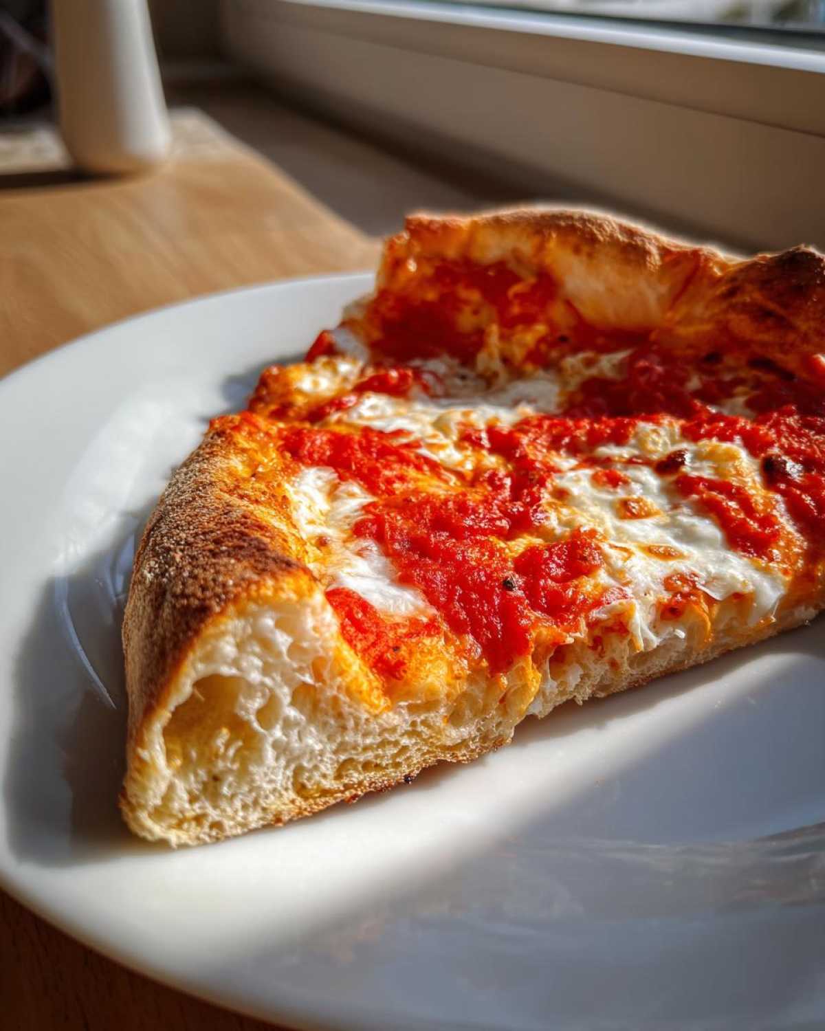 Close-up of a perfect pizza slice showing airy crust, bright red sauce, and melted mozzarella cheese.