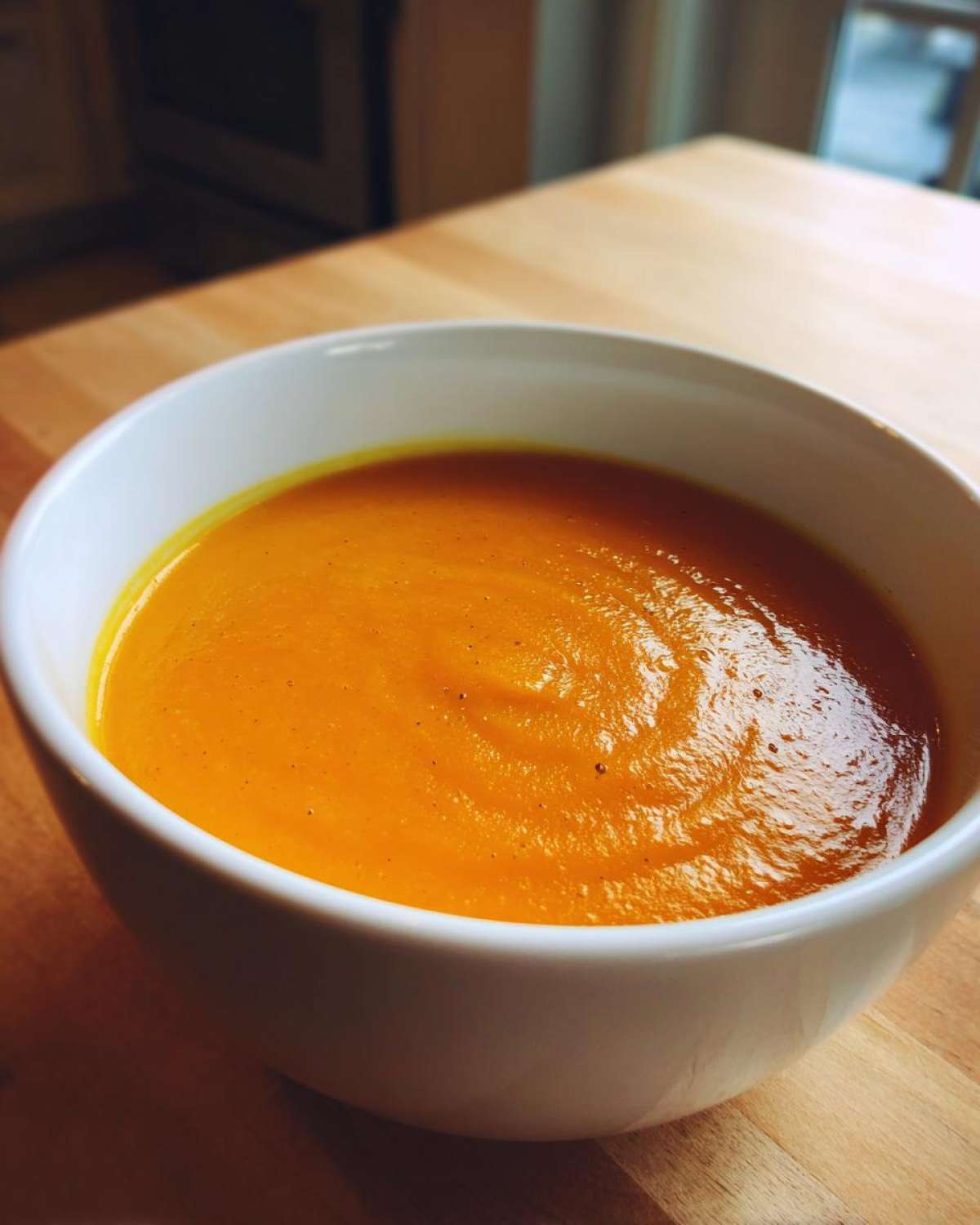 A close-up view of a vibrant orange bowl of smooth Roasted Butternut Squash Soup.