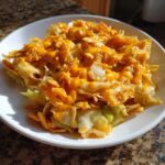 A white bowl filled with Frito Cowboy Cabbage, topped with melted orange cheese and crispy Fritos.