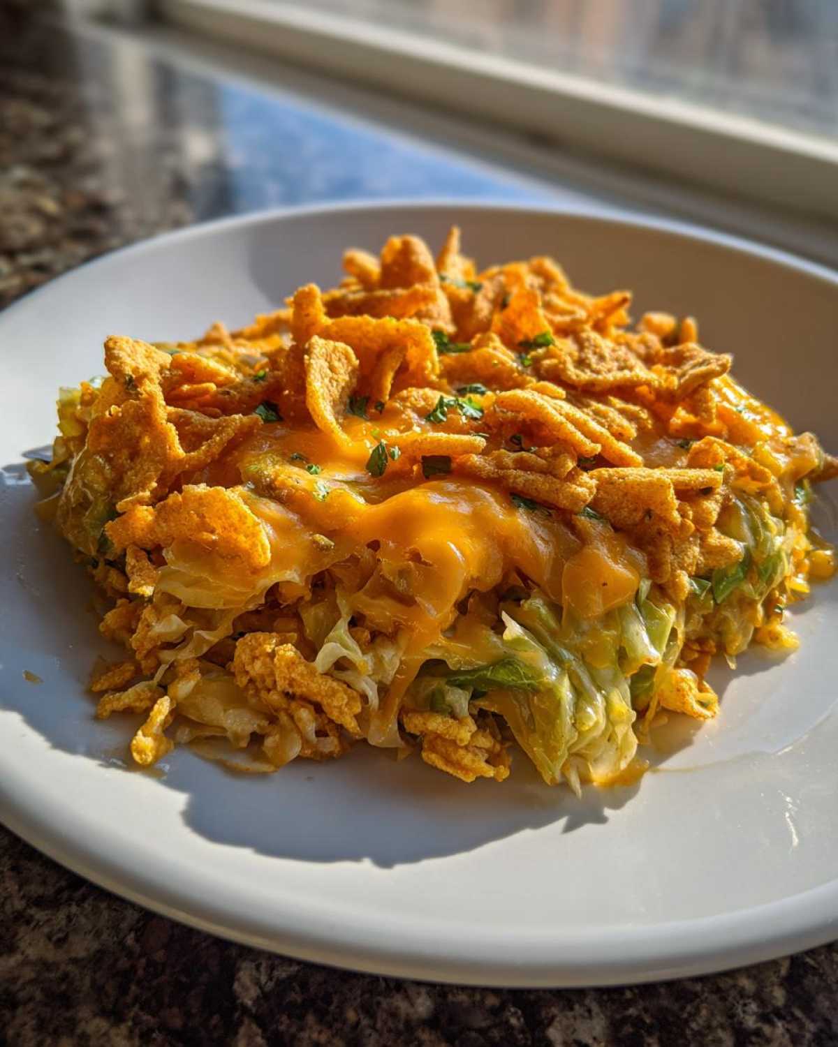 A close-up serving of Frito Cowboy Cabbage on a white plate, topped with melted cheddar cheese and crunchy Fritos.