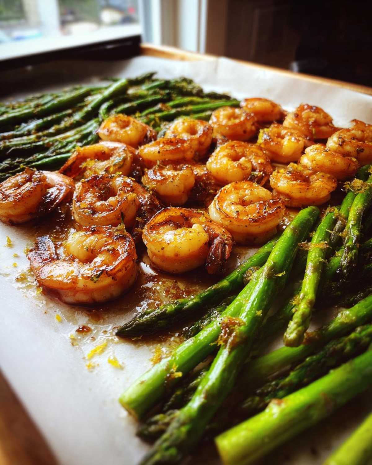 Close-up of Sheet Pan Crispy Garlic Butter Shrimp and Asparagus glistening with butter sauce on parchment paper.
