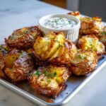 A pile of golden brown Sheet Pan Crispy Smashed Potatoes garnished with parsley, served with a small bowl of garlic aioli.