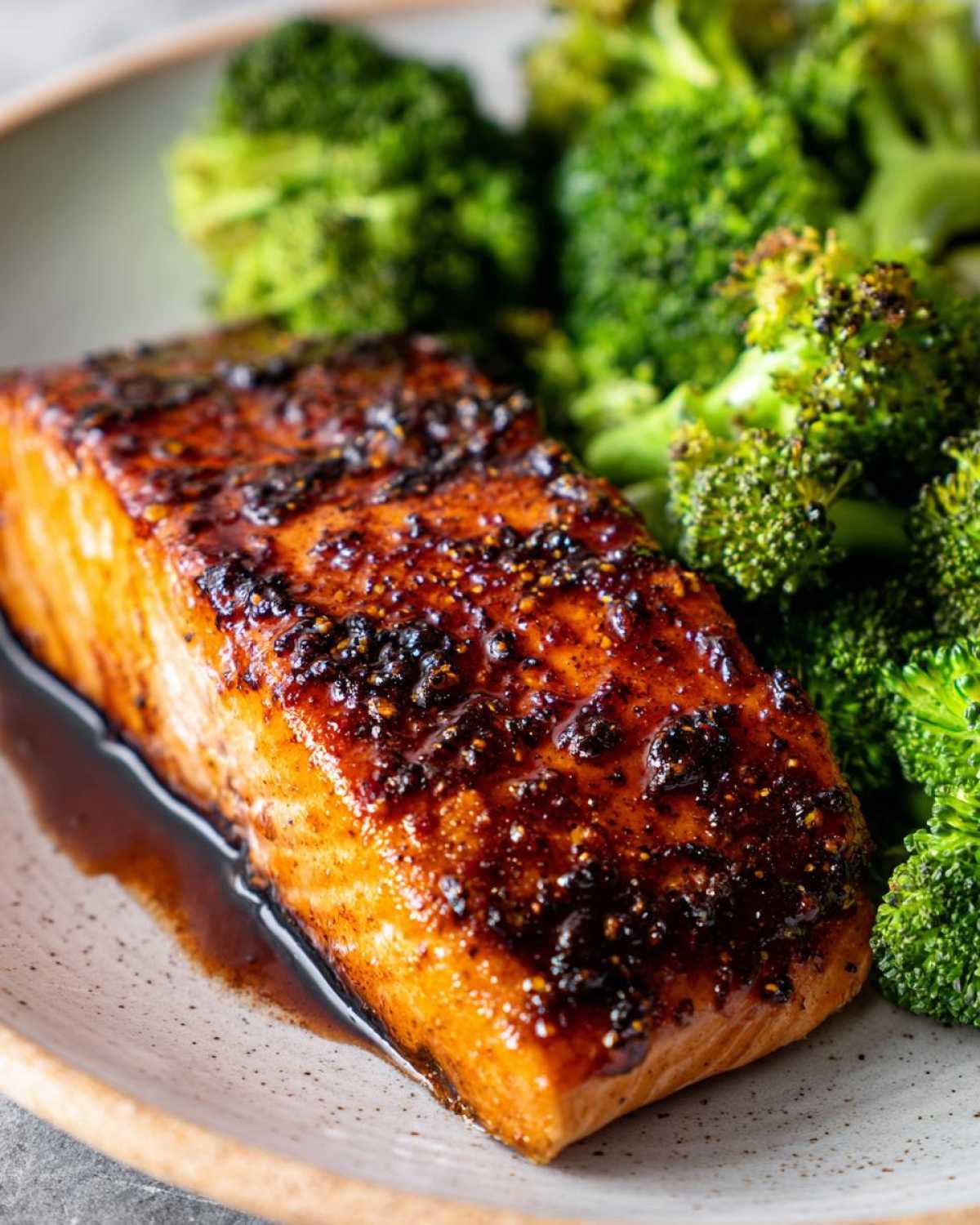 Close-up of a perfectly cooked fillet of Sheet Pan Honey Harissa Salmon with a dark, sticky glaze next to bright green roasted broccoli.