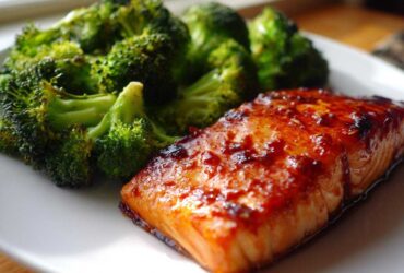 A close-up of a glazed Sheet Pan Honey Harissa Salmon fillet served next to bright green roasted broccoli florets on a white plate.
