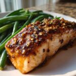 Close-up of a perfectly cooked salmon fillet topped with honey mustard glaze and sesame seeds, served with bright green beans.