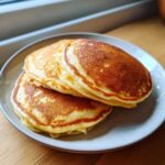 Three golden-brown, perfectly cooked pancakes stacked on a speckled plate, representing the Soft & Fluffy Brunch Favorite.