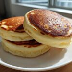 Three thick, golden-brown Japanese-style pancakes stacked on a white plate, showcasing the Soft & Fluffy Brunch Favorite texture.