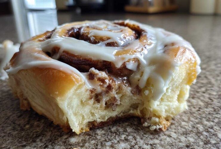 A close-up of one soft, fluffy cinnamon roll topped with thick white icing, showing a bite taken out.
