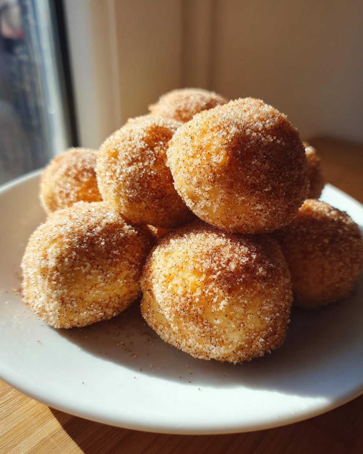 A close-up of several Soft & Sweet Cinnamon Sugar Biscuit Bites piled high on a white plate, coated in sparkling cinnamon sugar.