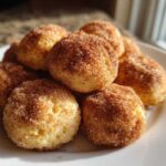 A close-up of several Soft & Sweet Cinnamon Sugar Biscuit Bites piled on a white plate, coated in cinnamon sugar.