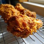 Close-up of crispy golden Southern Fried Chicken resting on a wire rack, showing its highly textured coating.