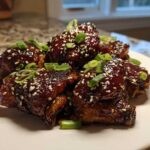 Close-up of Sticky Honey Chicken pieces glazed dark brown and topped with sesame seeds and green onions.