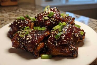 Close-up of Sticky Honey Chicken pieces glazed dark brown and topped with sesame seeds and green onions.