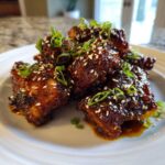 Close-up of Sticky Honey Chicken Irresistibly glazed wings garnished with sesame seeds and green onions on a white plate.