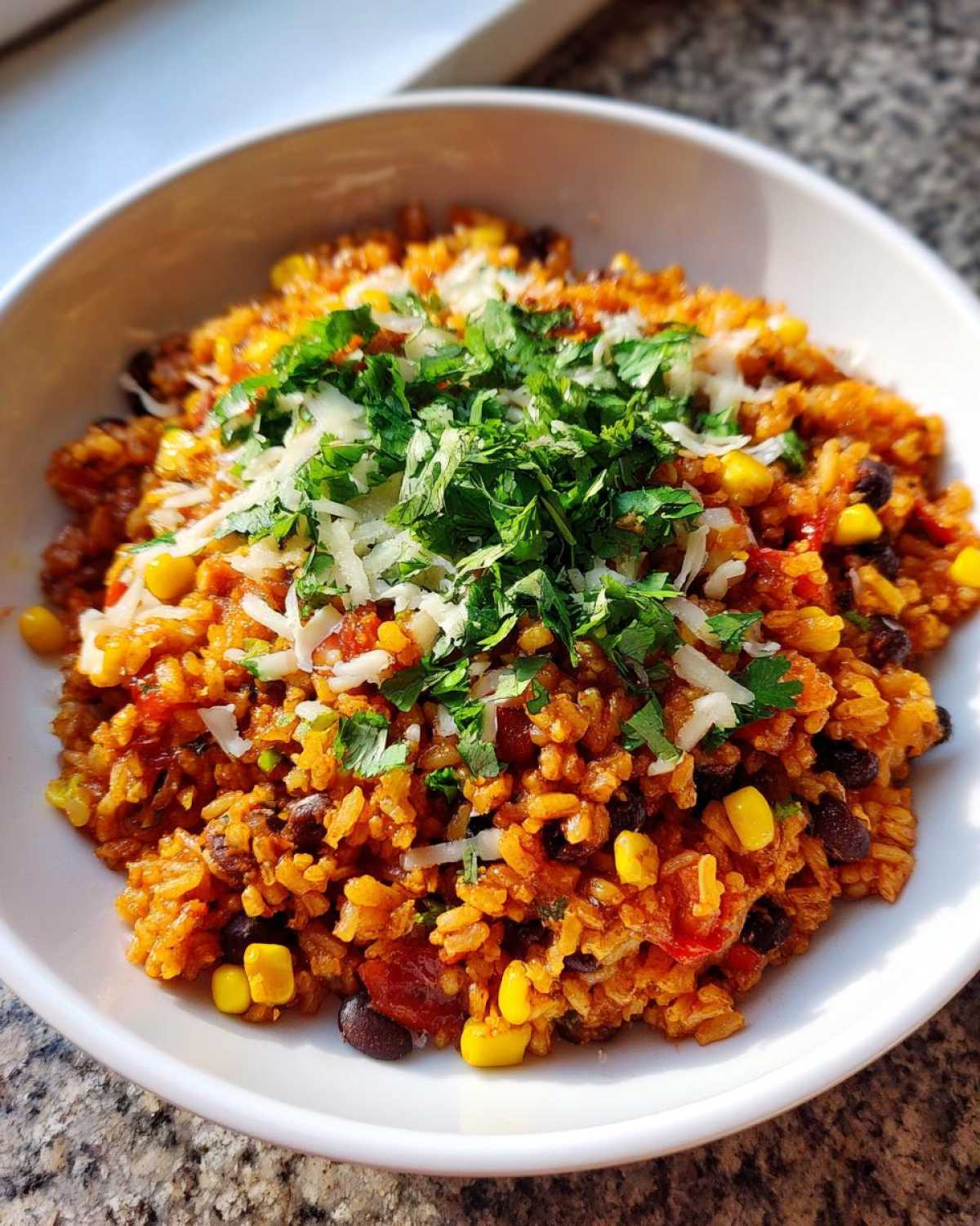 A close-up of a bowl filled with Tasty Salsa Rice mixed with black beans and corn, topped with shredded cheese and fresh cilantro.