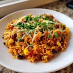 A close-up of a serving of Tasty Salsa Rice mixed with black beans and corn, topped with shredded cheese and fresh cilantro.