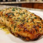 Close-up of a perfectly cooked Texas Roadhouse Salmon fillet topped with garlic butter and fresh parsley.
