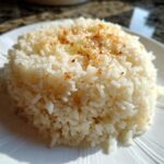 Close-up of a mound of fluffy Texas Roadhouse Seasoned Rice topped with melted butter and seasoning on a white plate.